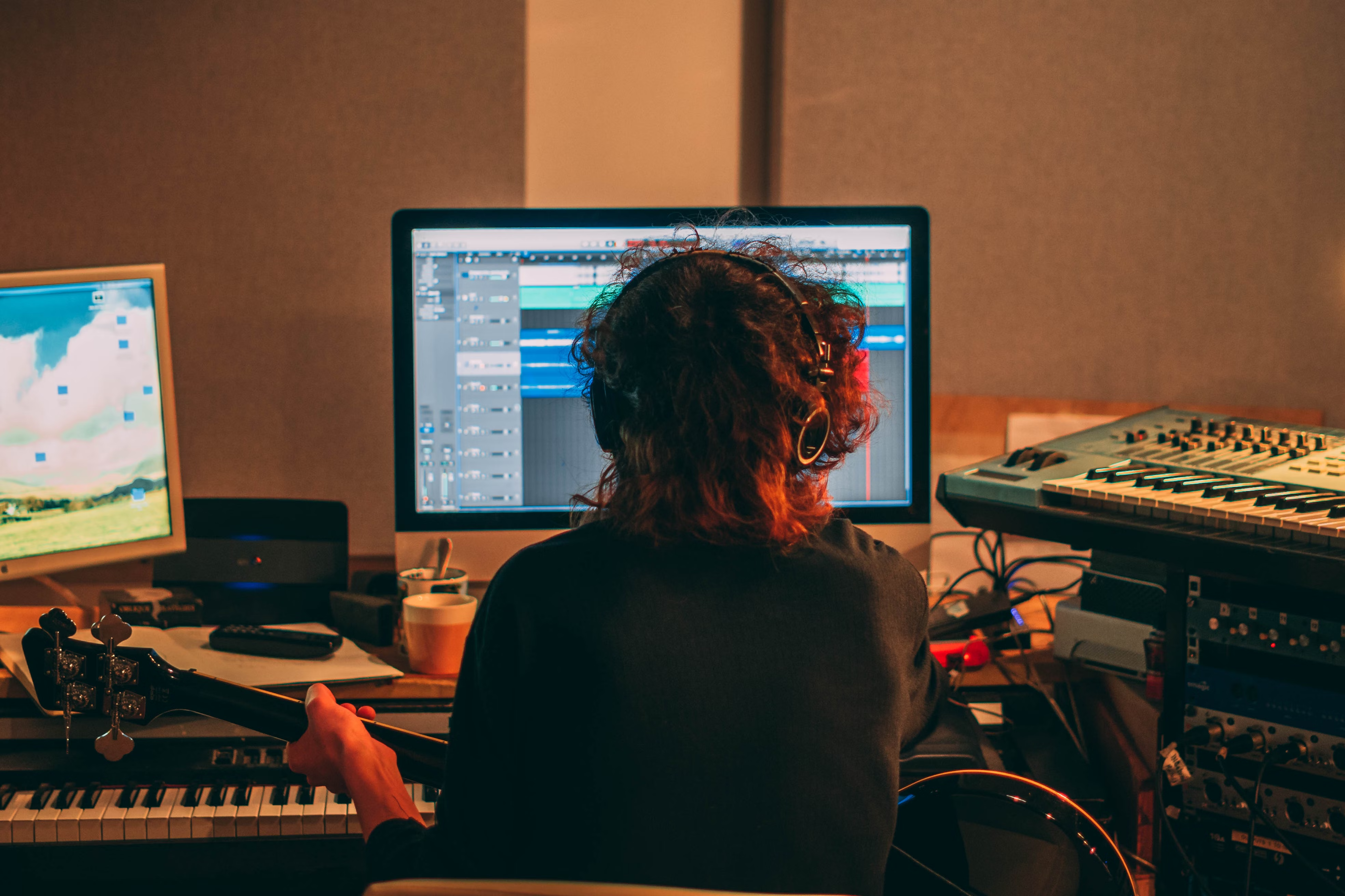 Person sitting at their computer with their guitar, trying to understand the difference between master and sync license